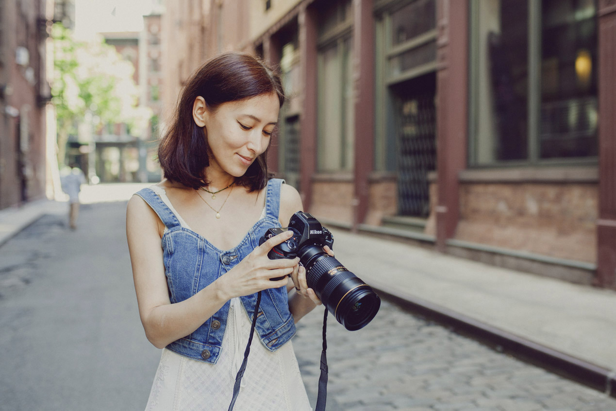 Baby Photography, woman with dark hair holding a camera is standing in the streets of Manhattan