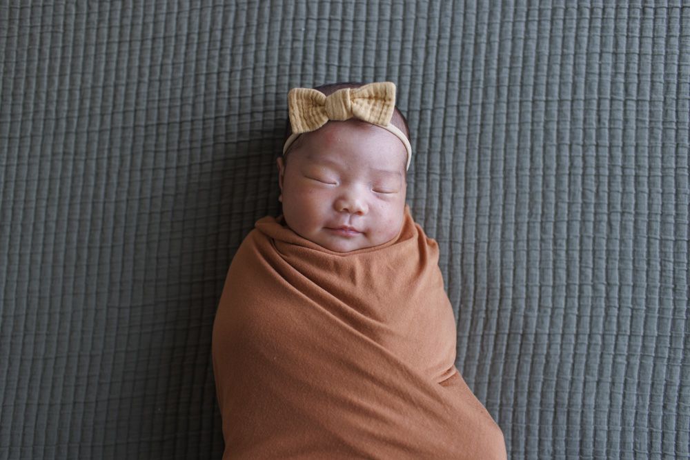 Baby Session, sleeping smiling newborn wrapped up in a blanket wearing a yellow bow lying on a green blanket