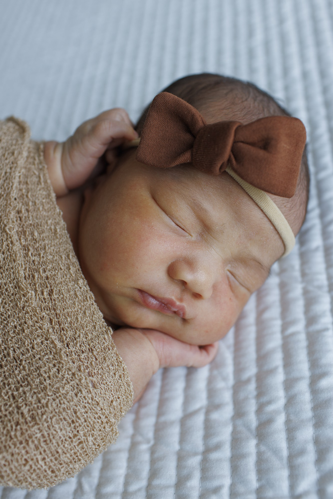 Newborn Session, close up of a swaddled newborn baby girl lying on white sheets wearing a headband with a big bow