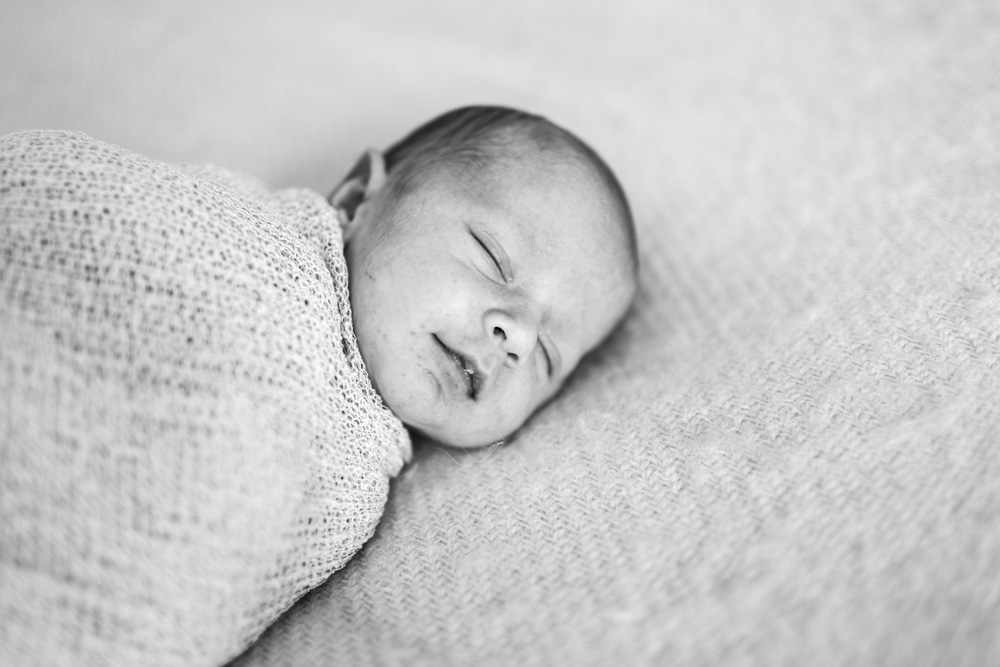 Baby Photography, black and white photo, close up of newborn swaddled in a blanket with smiling with its eyes closed