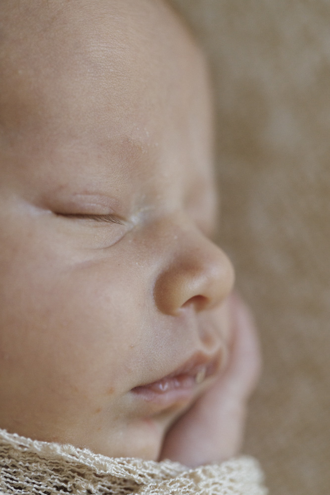 Baby Photography, close up of a sleeping newborn baby lying on a beige sheet swaddled in a beige blanket