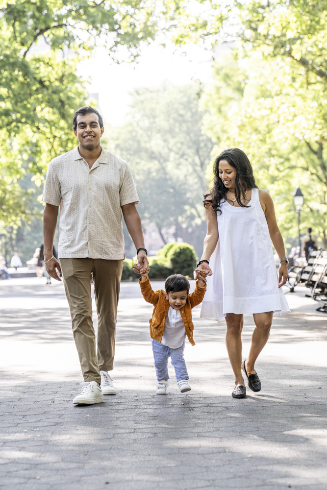 Family Photos, family of three is walking in a park, toddler is walking in the middle, they are holding hands