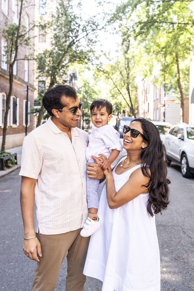 Family Photos, family of three standing in the streets of New York, father is holding his toddler while mother is looking at her son holding his hand, all are smiling
