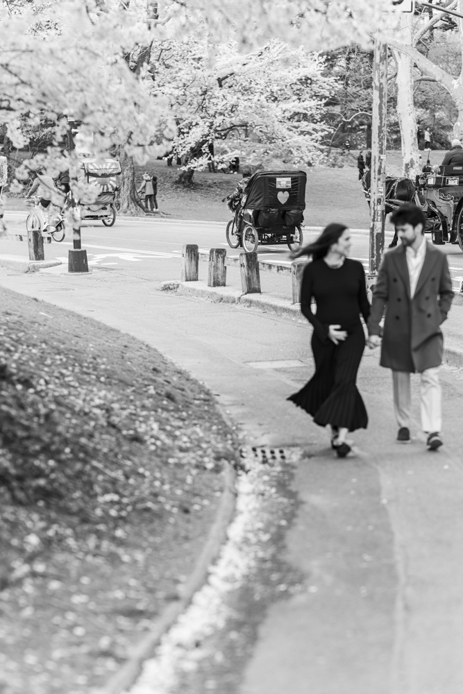 Maternity Photography, black and white photo of pregnant woman in a beautiful long black dress and her partner walking in a park holding hands and looking at each other while woman is holding her belly