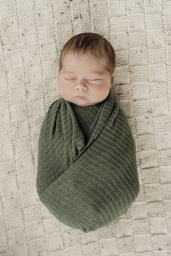 Baby Photography, close up of a sleeping newborn swaddled in a green blanket lying on a beige blanket