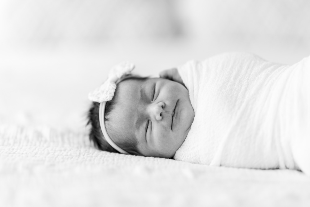 Newborn Session, black and white photo of sleeping smiling baby wearing a headband swaddled in a blanket lying on her side