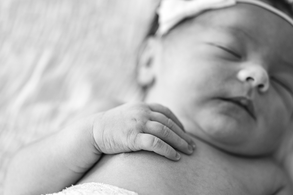 Newborn Session, black and white photo, close up of sleeping baby wearing a bow with hand on her chest