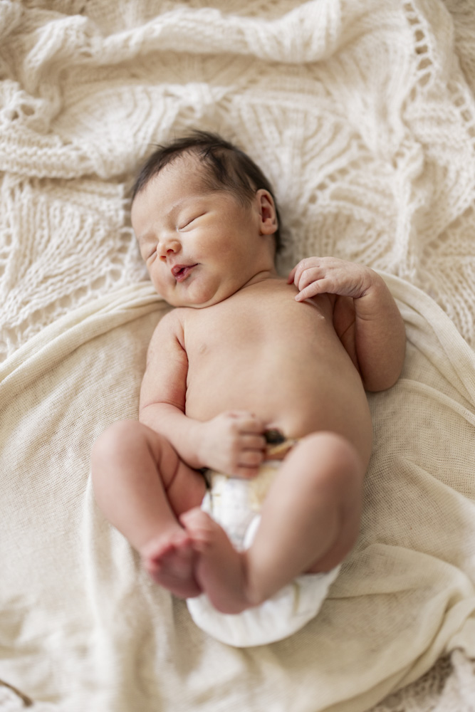 Baby Session, sleeping newborn in diapers is lying on a beige blanket with its feet up in the air