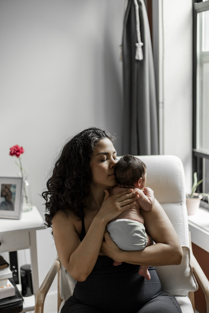 Newborn Photography, mom is sitting in a chair next to the window holding her newborn baby close to her face