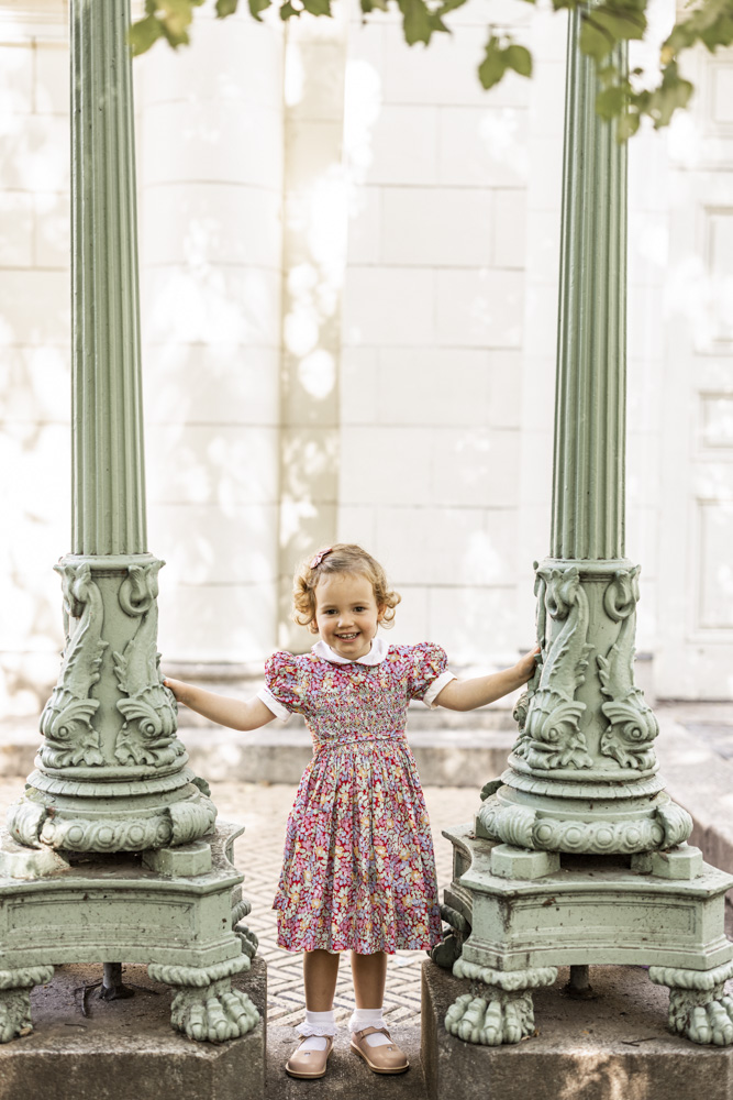 Family Session, cute little girl in a beautiful dress is standing between two pillars smiling at the camera